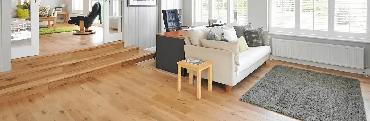 A modern living room with professionally installed laminate flooring, a beige sofa, a small side table, a gray rug, and large windows with white shutters in Yonkers, NY